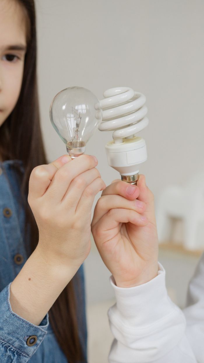 services-03 Two children comparing incandescent and CFL bulbs, highlighting differences in energy efficiency.